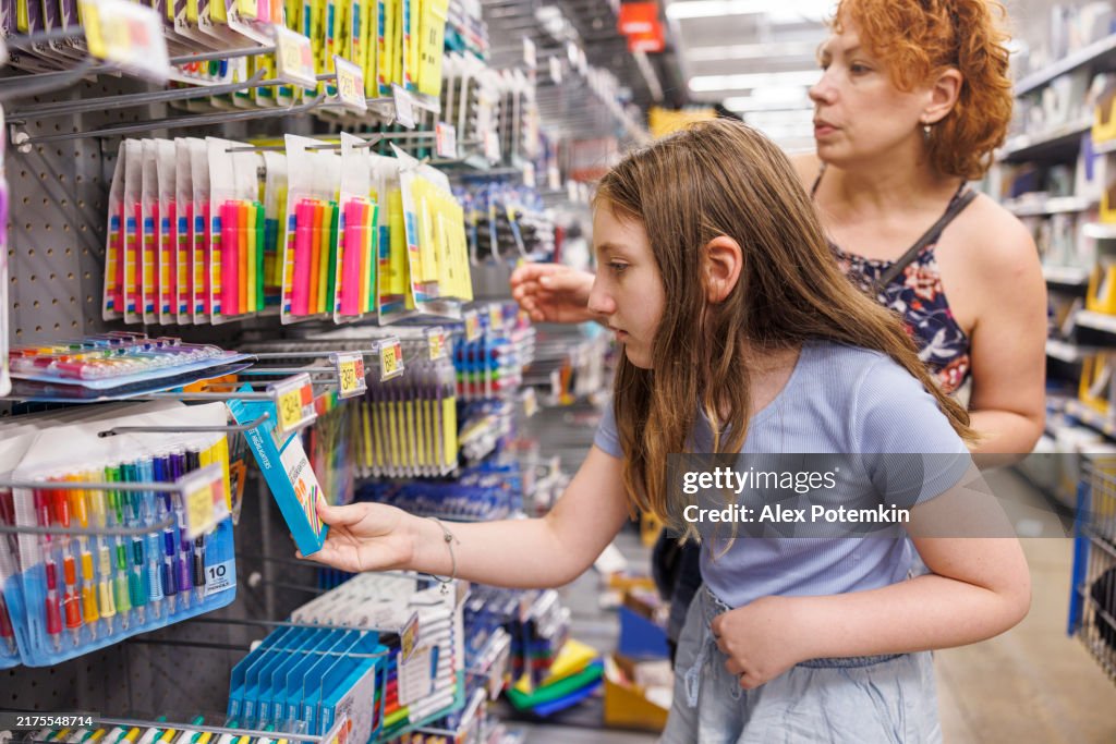Selecting school essentials together. Mother guides daughter through colorful stationery aisle.