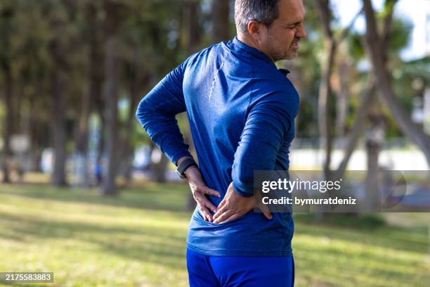 mid-aged man experiencing lower back pain - lower back stock pictures, royalty-free photos & images