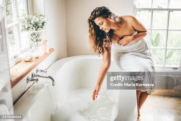 a woman wrapped in a towel fills a bathtub. - riempire foto e immagini stock