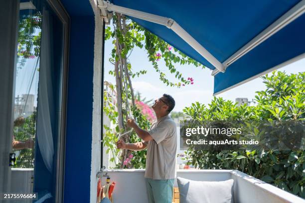 mann schließt die markise seiner terrasse - markise stock-fotos und bilder