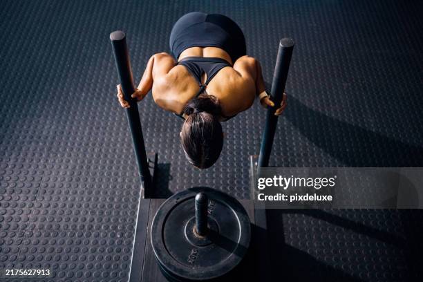 female athlete pushing a weighted sled in a gym. top view of a woman performing strength training exercise on a black gym floor. hyrox training concept. - sled push workout stock pictures, royalty-free photos & images