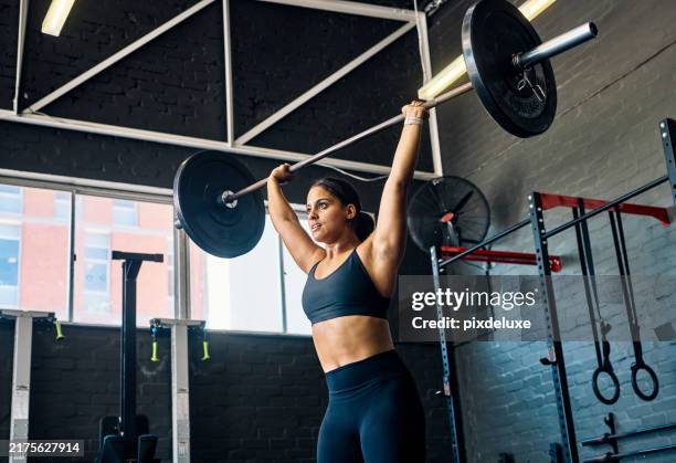 atleta femenina levantando pesas pesadas por encima de la cabeza en un gimnasio. vista lateral de una mujer realizando ejercicios de levantamiento de pesas en un gimnasio. - culturismo fotografías e imágenes de stock
