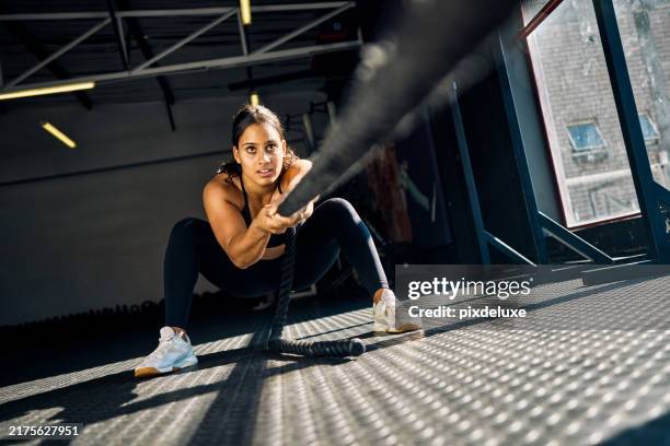 female athlete pulling a weighted sled in a gym. front view of a woman performing strength training exercise on a black gym floor. hyrox training concept. - effort stock pictures, royalty-free photos & images