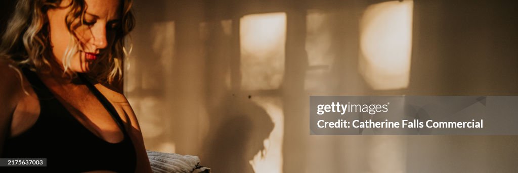 Conceptual banner image of a woman sitting indoors in evening light, casting shadows on the wall, experiencing a moment of reflection and tranquility