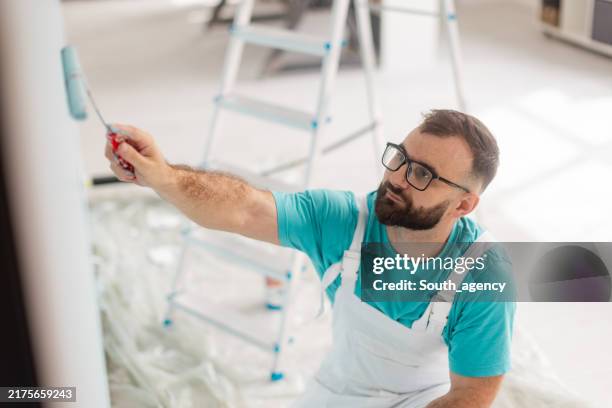 man painting wall with roller, ladder in background - decorating stock pictures, royalty-free photos & images