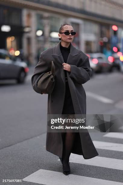 Anna Wein is seen wearing black oval sunglasses; chunky squared earrings in gold with a black stone from H&M Studio; an oversized ankle-length grey...