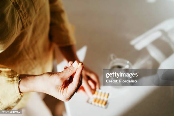 a woman standing at a table with green pills in her hand - ormone foto e immagini stock