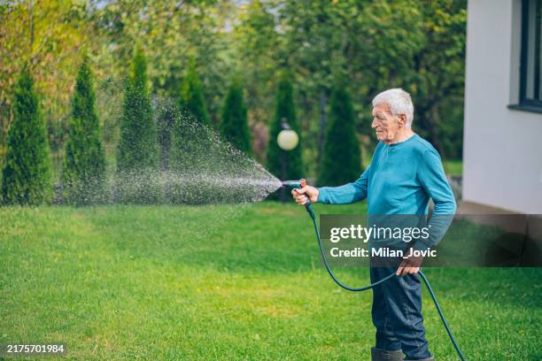 älterer mann bei der bewässerung des gartens mit gartenschlauch - wasserschlauch stock-fotos und bilder