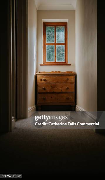 small, narrow hallway with a chest of drawers underneath a small window - enge stock-fotos und bilder