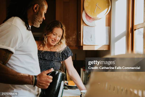 couple enjoying morning coffee together in a sunlit kitchen while preparing breakfast - boiling stock pictures, royalty-free photos & images