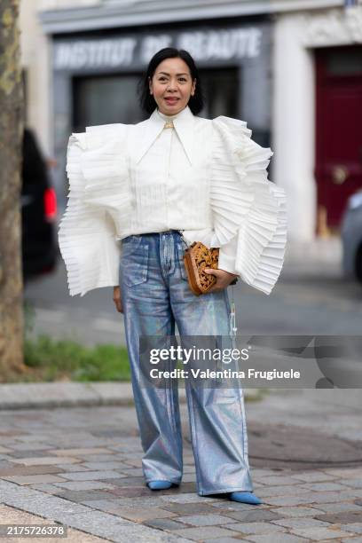 Guest wears blue pumps, a brown bag, silver denim jeans and a puffy sleeves white shirt outside Stella McCartney show during Womenswear Spring/Summer...