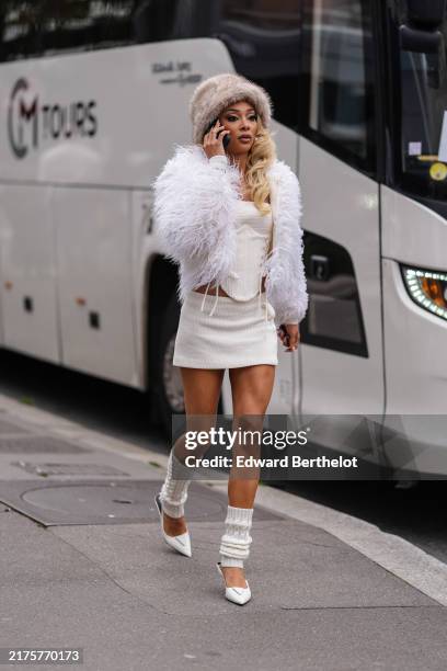 Guest wears light brown fluffy bucket hat, white fluffy jacket, white laced side corset top, white mini skirt, white knit warmers, white pointed toe...