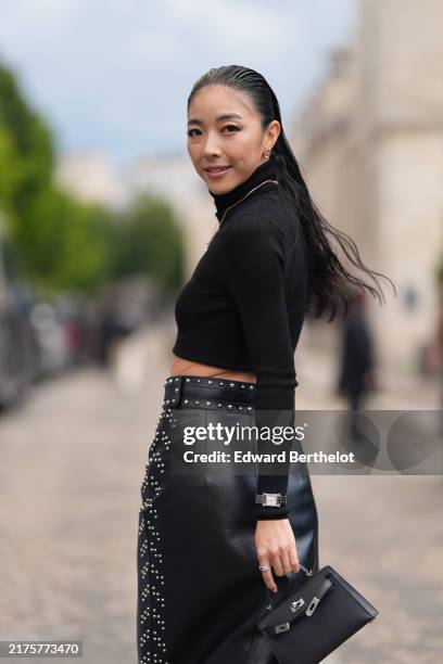 Yuwei Zhangzou wears black turtleneck long sleeve cropped shirt, silver necklace, shiny black high waisted over studded high slit Hermes leather midi...