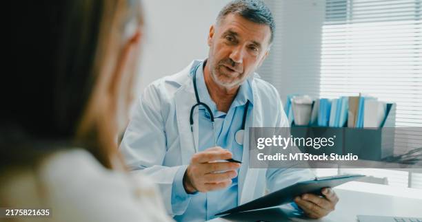 senior doctor in lab coat using digital tablet discusses medical test results with a patient in clinical office. medical health care. - medical examination stock pictures, royalty-free photos & images