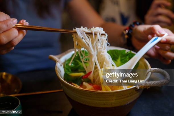 une vue rapprochée d’un bol fumant de nouilles à la citronnelle épicées et acidulées. le plat est vibrant avec de l’huile de piment rouge flottant à la surface, de fines nouilles immergées dans le bouillon aromatique et garnies d’herbes fraîc - cuisine thaïlandaise photos et images de collection
