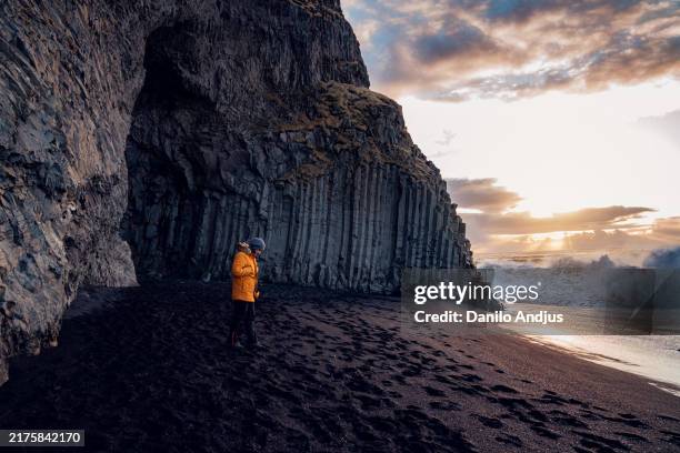 an explorer standing on a black sand beach and looking at the powerful waves - schwarzer sand stock-fotos und bilder