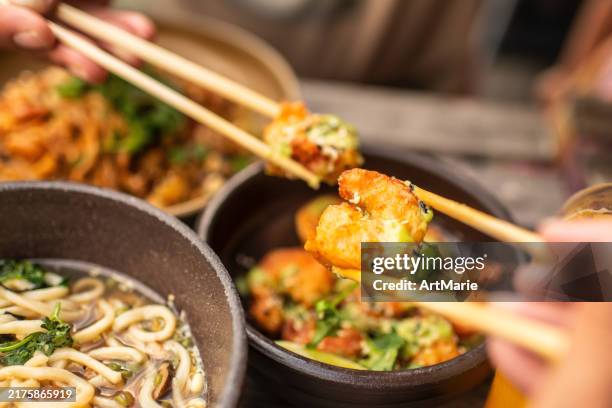 people eating tempura shrimps, ramen and singapore noodles in a cafe - wok stockfoto's en -beelden