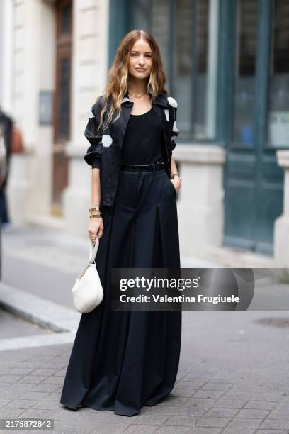 Victoria Magrath wears gold earrings, a gold necklace, a black tank top, a black and white polka dots printed jacket, a black leather belt, a black...