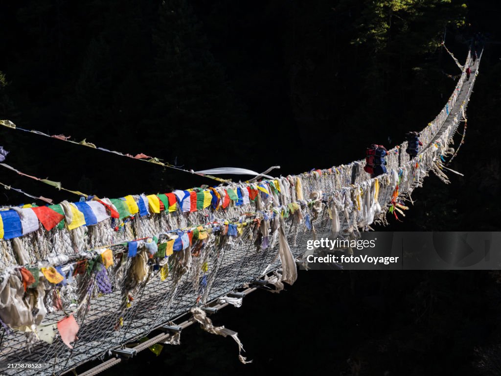 Sherpa porters crossing wire bridge with prayer flags Himalayan mountains
