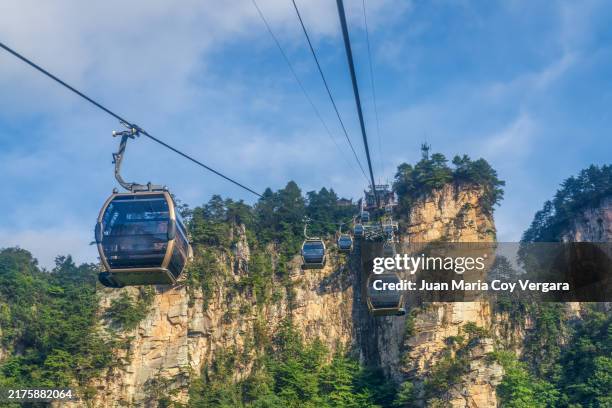 eye level view cable cars carry visitors over the towering cliffs of zhangjiajie national forest park in china. the cable car's personal perspective of the dramatic rock formations and lush greenery provides a breathtaking aerial view of this park - zhangjiajie stock pictures, royalty-free photos & images
