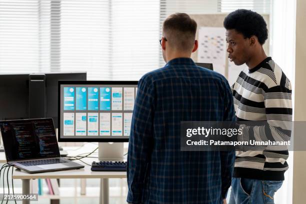two app developers engage in a collaborative discussion about new code developments for building mobile applications, with a phone screen template displayed on a computer monitor. captures a tech-focused work environment where expertise in coding. - application programming stock pictures, royalty-free photos & images