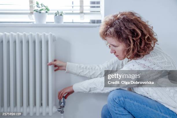 a woman adjusting the thermostat valve on a heating radiator - energy bill stock pictures, royalty-free photos & images