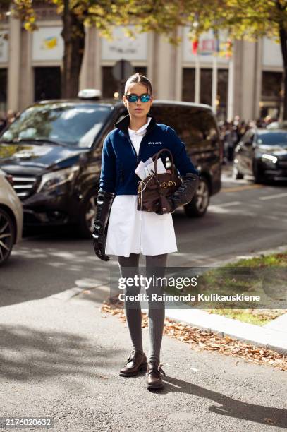Guest wears grey tights, white mini dress, blue jacket and brown bag outside the Miu Miu show during Womenswear Spring/Summer 2025 as part of Paris...