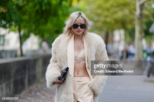 Guest wears black sunglasses, cream faux fur coat, cream bralette, outside Zimmermann, during the Paris Fashion Week Spring/Summer 2025 on September...