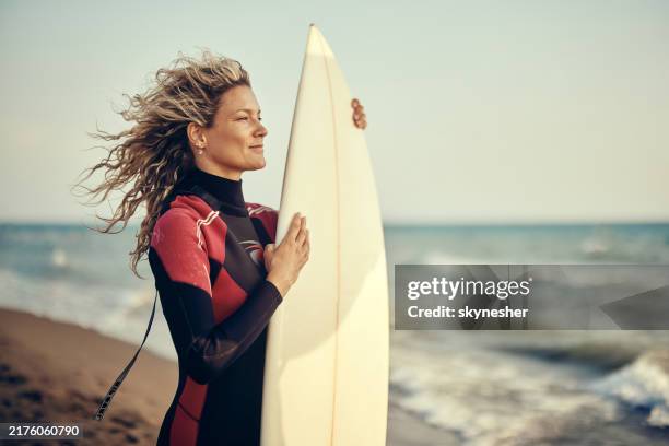 smiling female surfer looking at waves from the beach. - surfer stock pictures, royalty-free photos & images