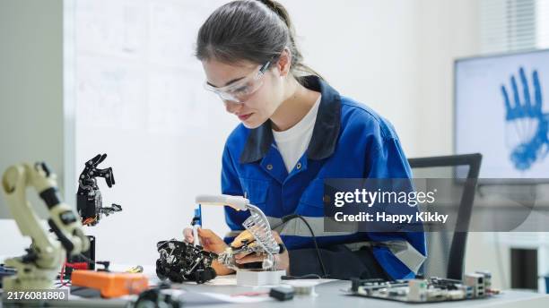 white woman engineer developer wearing safety protective goggles with blue work jacket is soldering intricate robotic components on a circuit board or an electronic device workshop in a laboratory room - soldering robot stock pictures, royalty-free photos & images