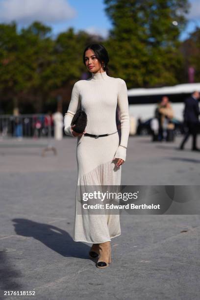 Kelsey Merritt wears white high neck long sleeve sheer mesh midi dress, black leather belt, shiny black quilted Chanel leather bag, light brown suede...