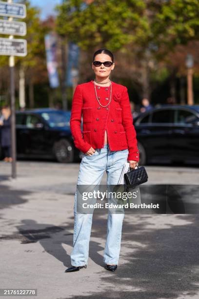 Guest wears black sunglasses, silver layered necklaces, bright red tweed Chanel blazer jacket, washed light blue denim jean pants, shiny black...