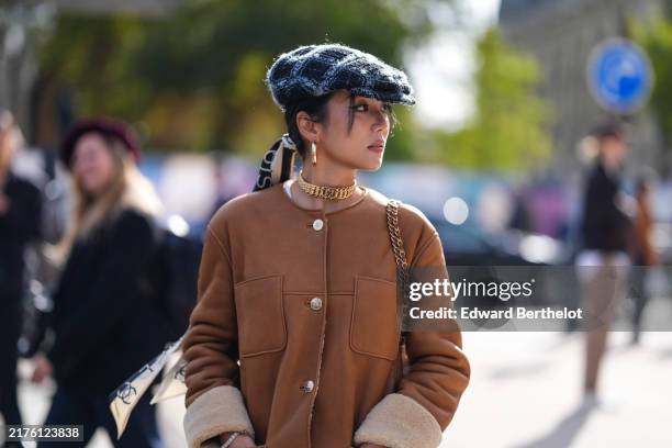 Yoyo Cao wears dark blue light blue hat, gold hoop earrings, gold choker necklace, dark brown oversized leather coat with light brown fluffy cuffs,...