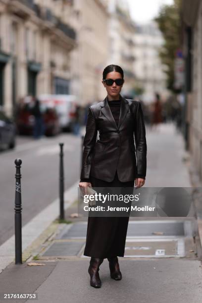 Christina Najjar is seen wearing a long black dress with a stand-up collar, a long black leather blazer, black leather boots, black sunglasses and a...