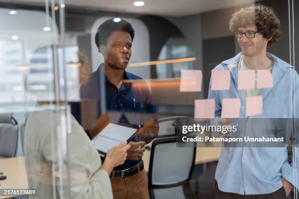 head of product development standing in a meeting room, discussing ideas with a multiracial team while posting adhesive notes on the glass wall. the session focuses on analyzing market data, creating strategies, and driving business innovation. - startup services growth images stock pictures, royalty-free photos & images