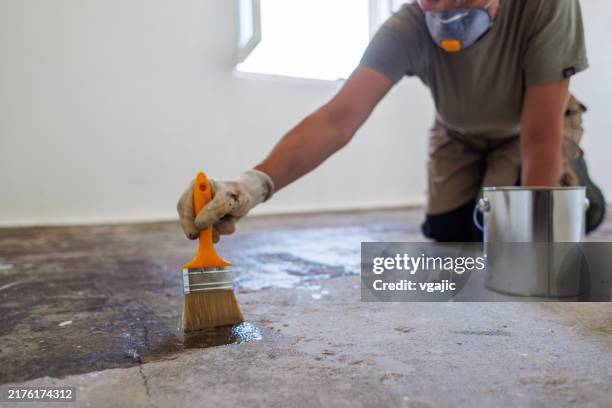 female worker applying protective coating to a concrete floor in renovation project - sealant stock pictures, royalty-free photos & images