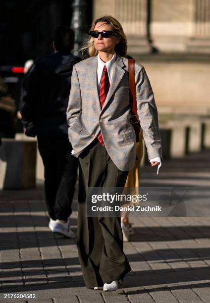 Guest is seen wearing a gray jacket, white shirt, red tie, gray pants and white heels with black sunglasses outside the Louis Vuitton show during...