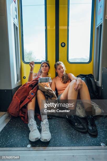 young women backpackers sitting on floor on train - rugzaktoerist stockfoto's en -beelden