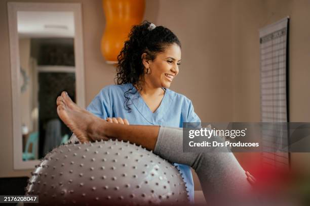 elderly patient doing physical therapy on her leg with a swiss pilates ball - physical therapist stock pictures, royalty-free photos & images