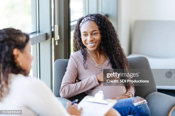 cheerful young pregnant woman listens to unrecognizable female counselor - pregnancy stock pictures, royalty-free photos & images