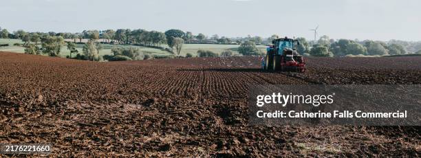 tractor plowing farmland in the countryside on a clear day with green trees in the background - farm to table stock pictures, royalty-free photos & images
