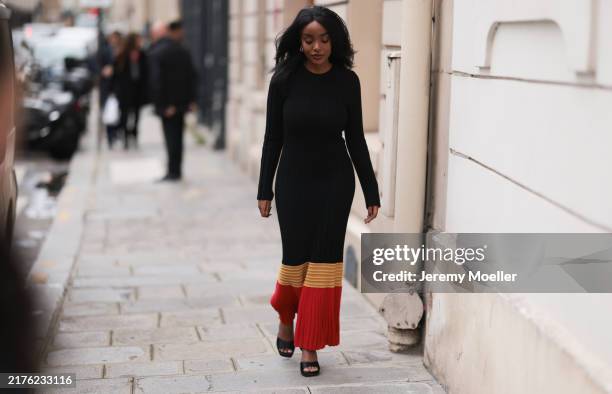Fashion Week guest is seen wearing chunky gold hoop earrings; a long-sleeved maxi dress with high round neckline, mainly in black with red and yellow...