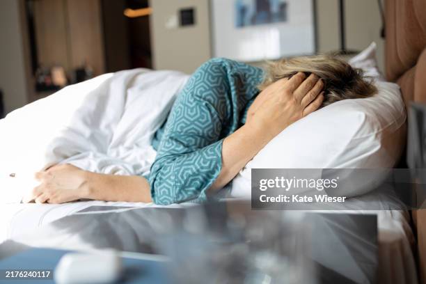 mature woman in depression lying in bed covered with blanket. - krankenbett stock-fotos und bilder