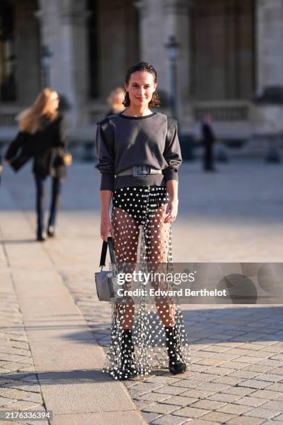 Alicia Vikander wears dark gray black long sleeve Louis Vuitton shirt, black leather Louis Vuitton belt, black Louis Vuitton mini shorts, white sheer...