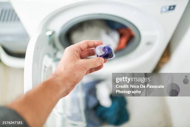 close up of hand holding detergent capsule in front of washing machine - weidenkätzchen stock-fotos und bilder