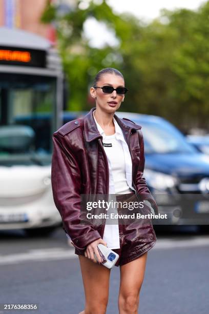 Guest wears black sunglasses, cream tank top, white unbuttoned long sleeve shirt, shiny dark red oversized biker leather jacket, dark brown leather...