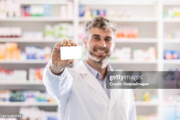 a young pharmacist in a pharmacy holds a blank white loyalty card in his hand. - prämienkarte stock-fotos und bilder