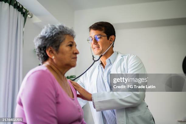 doctor listening senior patient woman's heartbeat during consultation at hospital - lunga bildbanksfoton och bilder