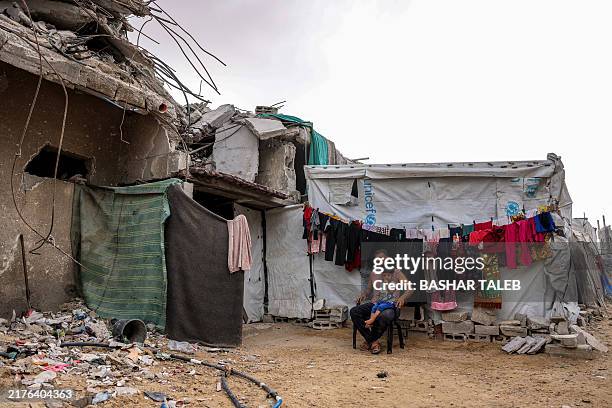 Man sits with a child next to drying clothes on a laundry line outside a tent shelter erected next to a destroyed building in Khan Yunis in the...