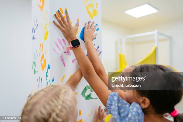 gruppe von mädchen, die handabdrücke an der wand im kinderspielzimmer hinterlassen - handabdruck stock-fotos und bilder